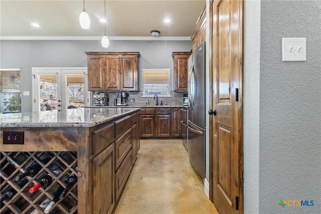 kitchen with light stone counters, a kitchen island, sink, pendant lighting, and stainless steel refrigerator