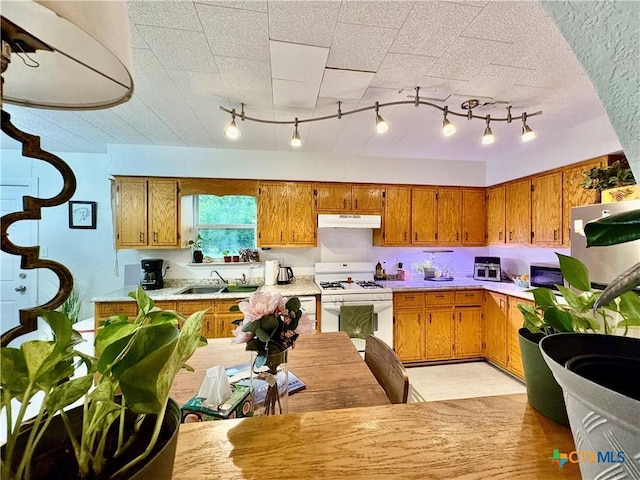 1003 Standifer St, Lampasas, TX 76550 - kitchen with white range with gas stovetop, under cabinet range hood, brown cabinetry, track lighting, and a sink
