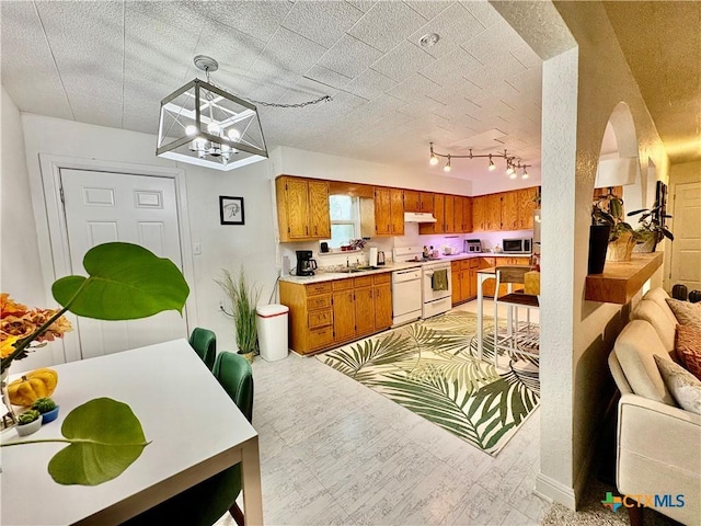 1003 Standifer St, Lampasas, TX 76550 - kitchen with under cabinet range hood, brown cabinetry, white range, light countertops, and dishwashing machine