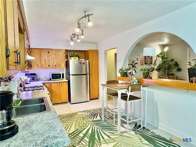 1003 Standifer St, Lampasas, TX 76550 - kitchen featuring freestanding refrigerator, brown cabinetry, light countertops, a sink, and under cabinet range hood