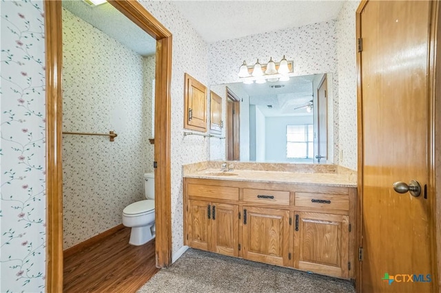 bathroom featuring vanity, wood finished floors, toilet, and wallpapered walls