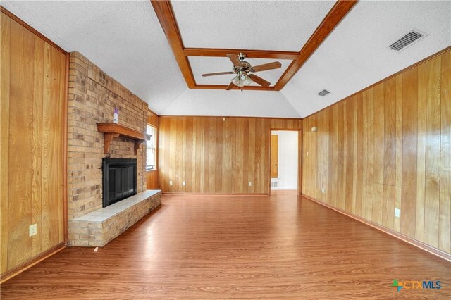 unfurnished living room featuring wooden walls, ceiling fan, visible vents, and wood finished floors