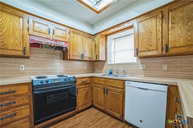 kitchen featuring a sink, dishwasher, light countertops, under cabinet range hood, and black range with electric stovetop