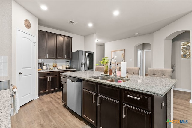 kitchen with light hardwood / wood-style floors, stainless steel appliances, sink, tasteful backsplash, and a kitchen island with sink