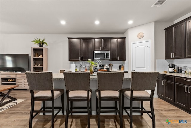 kitchen featuring light wood-type flooring, stainless steel appliances, a center island, and light stone countertops