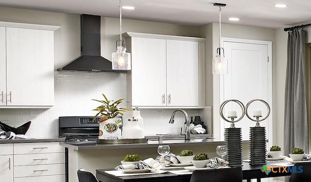 kitchen featuring white cabinets, wall chimney exhaust hood, stove, and decorative light fixtures