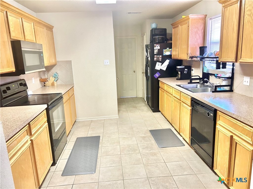 kitchen with black appliances, backsplash, light tile patterned floors, light brown cabinets, and sink