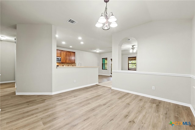 unfurnished living room with vaulted ceiling, ceiling fan with notable chandelier, and light hardwood / wood-style flooring