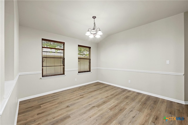 unfurnished room with light hardwood / wood-style flooring, a chandelier, and vaulted ceiling