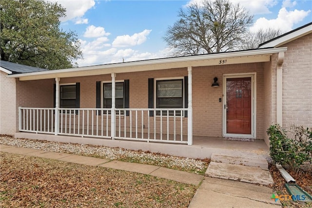 view of exterior entry with a porch and brick siding