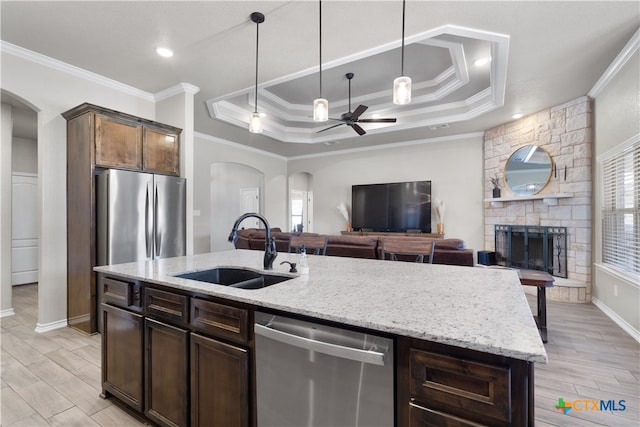 kitchen with dark brown cabinetry, sink, an island with sink, a fireplace, and appliances with stainless steel finishes