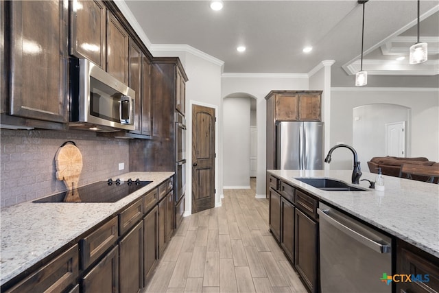 kitchen with light stone counters, ornamental molding, stainless steel appliances, hanging light fixtures, and sink