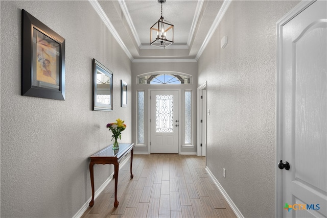 entryway with a tray ceiling, an inviting chandelier, hardwood / wood-style flooring, and crown molding