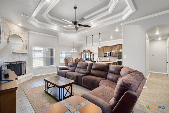 living room featuring ornamental molding, light hardwood / wood-style floors, a tray ceiling, and a stone fireplace