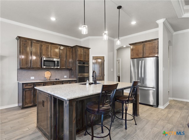 kitchen featuring a center island with sink, light stone counters, dark brown cabinets, appliances with stainless steel finishes, and decorative light fixtures