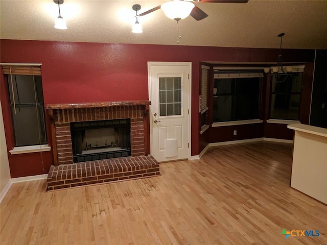 unfurnished living room with ceiling fan with notable chandelier, wood finished floors, and a fireplace