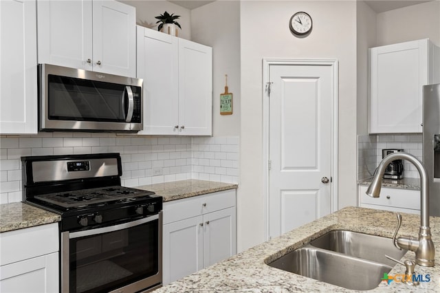 kitchen with decorative backsplash, appliances with stainless steel finishes, light stone countertops, white cabinetry, and a sink