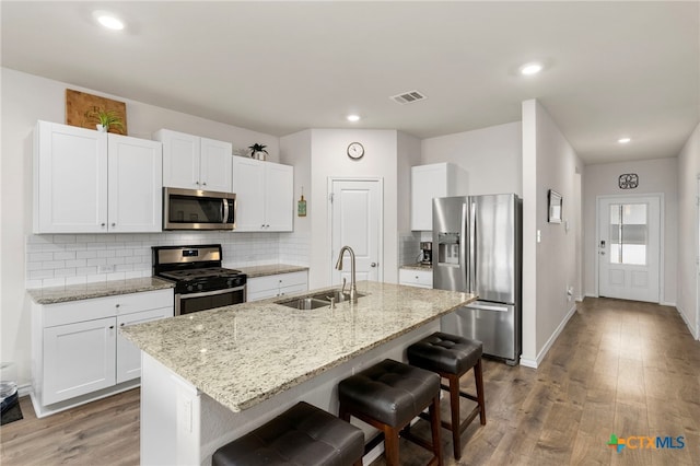 kitchen featuring stainless steel appliances, visible vents, a sink, wood finished floors, and a kitchen breakfast bar