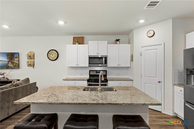 kitchen featuring visible vents, white cabinets, appliances with stainless steel finishes, a breakfast bar area, and light stone countertops