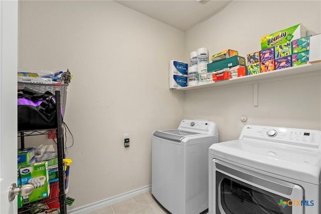 clothes washing area featuring laundry area, light tile patterned flooring, baseboards, and washing machine and clothes dryer