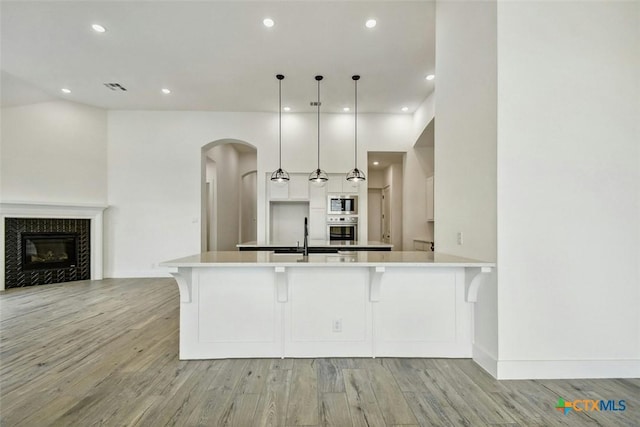 kitchen featuring pendant lighting, stainless steel oven, white cabinets, built in microwave, and a tiled fireplace