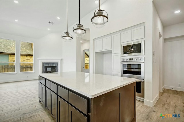 kitchen with white cabinetry, hanging light fixtures, light stone counters, light hardwood / wood-style flooring, and dark brown cabinets