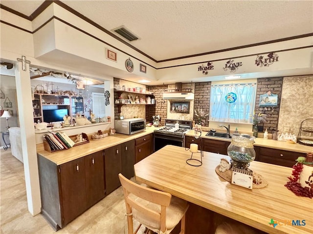 kitchen with a textured ceiling, visible vents, gas range, stainless steel microwave, and under cabinet range hood