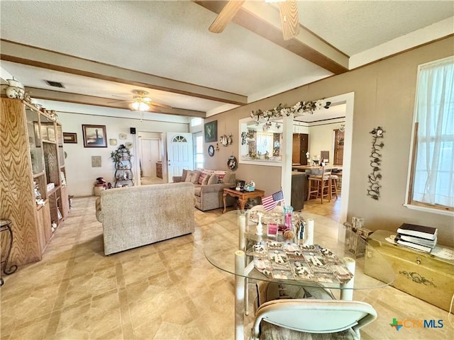 living room with beamed ceiling, visible vents, a textured ceiling, and a ceiling fan