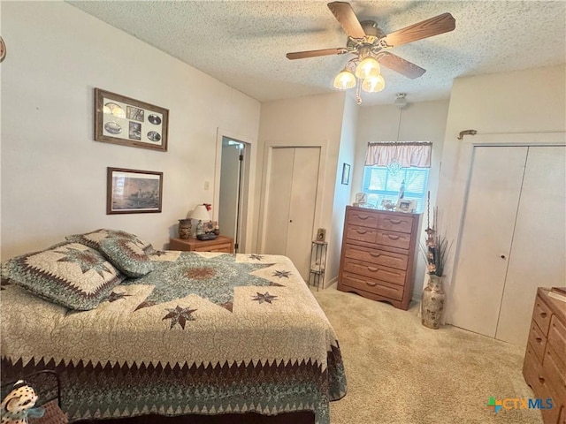 bedroom featuring light carpet, a textured ceiling, two closets, and a ceiling fan