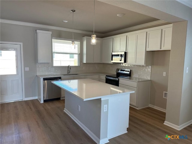 kitchen with appliances with stainless steel finishes, ornamental molding, dark wood-type flooring, a center island, and a sink