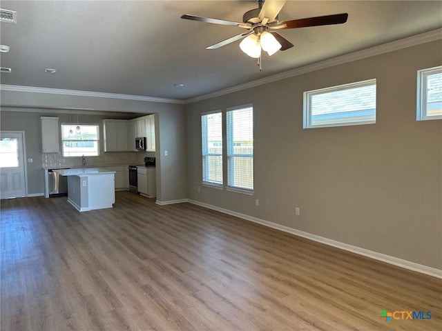 unfurnished living room featuring plenty of natural light, crown molding, and wood finished floors