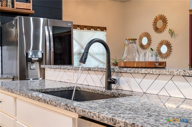 kitchen with a sink, stainless steel fridge, and light stone countertops