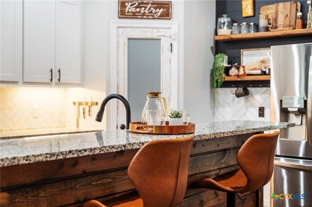 interior details with light stone counters, white cabinets, backsplash, stainless steel fridge with ice dispenser, and open shelves