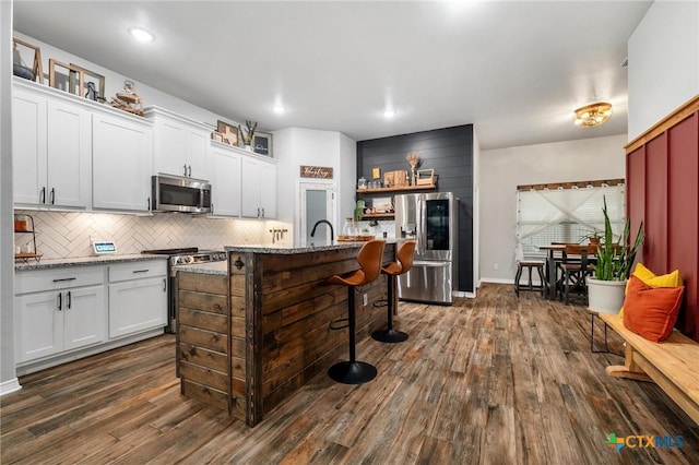 kitchen with stainless steel appliances, dark wood-style flooring, backsplash, and a breakfast bar area