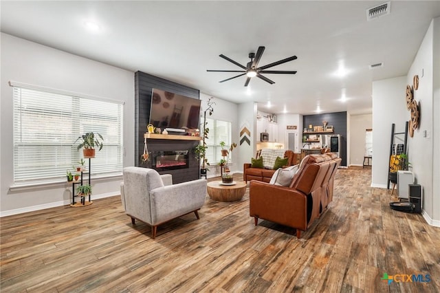 living area featuring a large fireplace, ceiling fan, visible vents, and wood finished floors