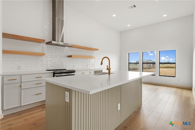 kitchen featuring a kitchen island with sink, wall chimney exhaust hood, white cabinetry, and light hardwood / wood-style floors