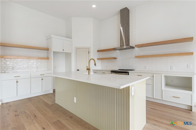 kitchen with tasteful backsplash, an island with sink, white cabinets, wall chimney exhaust hood, and light hardwood / wood-style flooring