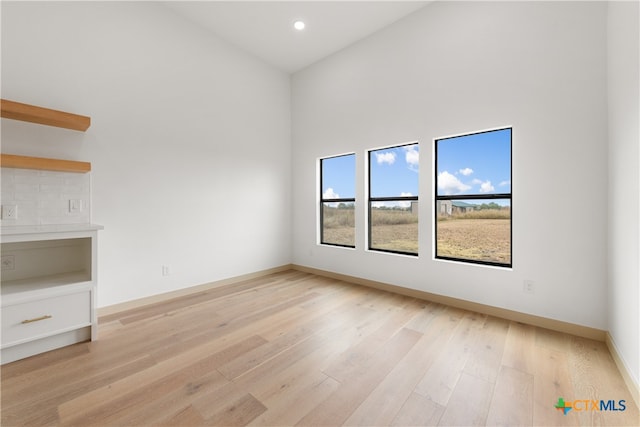 empty room featuring high vaulted ceiling and light wood-type flooring