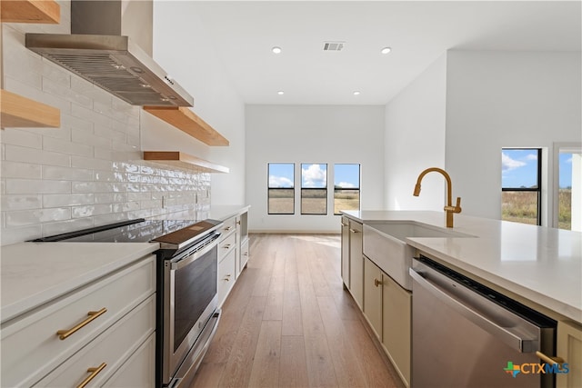 kitchen featuring stainless steel appliances, wall chimney range hood, a healthy amount of sunlight, and light hardwood / wood-style flooring