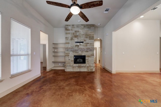 unfurnished living room with concrete floors, ceiling fan, and a stone fireplace