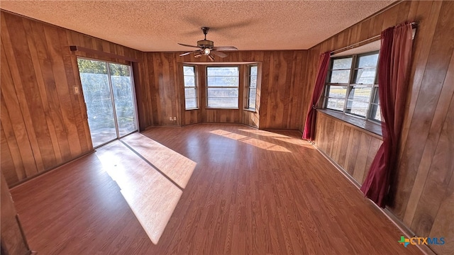 empty room featuring a textured ceiling, light wood-type flooring, ceiling fan, and wood walls