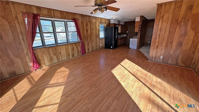 unfurnished living room with hardwood / wood-style floors, a textured ceiling, ceiling fan, and wood walls