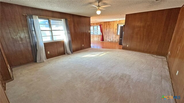 unfurnished room featuring ceiling fan, wood walls, light colored carpet, and a textured ceiling