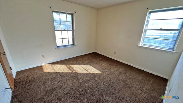 unfurnished room with plenty of natural light and dark carpet