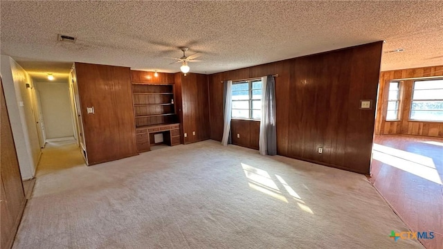 902 Holly St, Copperas Cove, TX 76522 - unfurnished living room with wood walls, a ceiling fan, a textured ceiling, carpet, and built in shelves