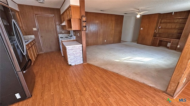 kitchen with a textured ceiling, light hardwood / wood-style floors, stainless steel refrigerator, and wood walls