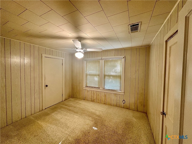 carpeted empty room with wooden walls and ceiling fan