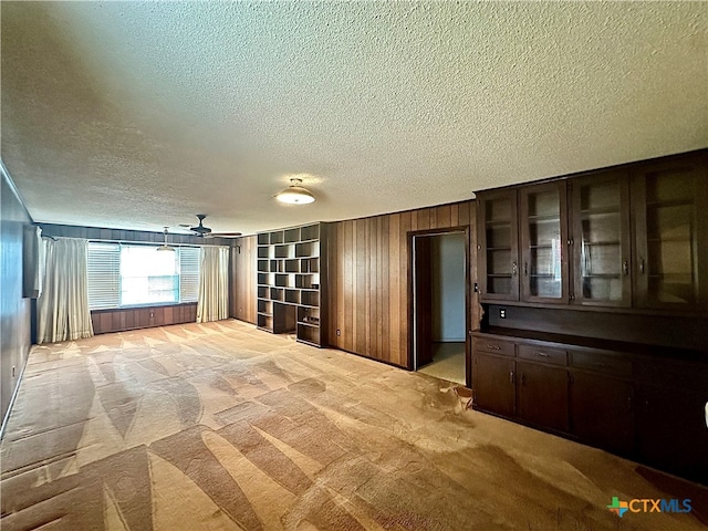 spare room with ceiling fan, light colored carpet, wooden walls, and a textured ceiling