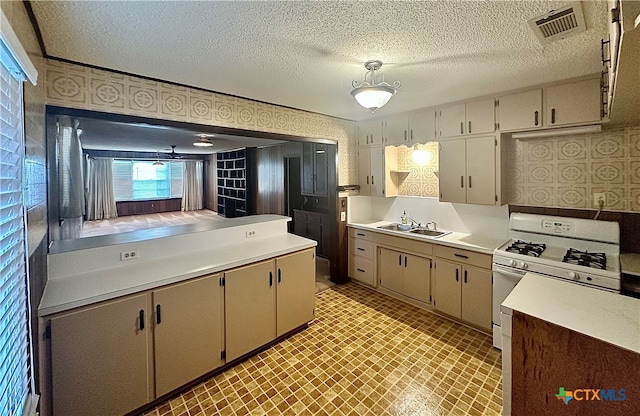 kitchen featuring white gas range, cream cabinetry, a textured ceiling, and sink