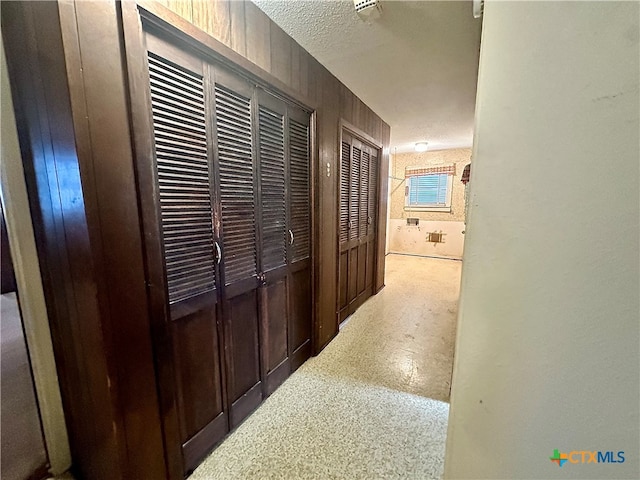 corridor featuring wooden walls and a textured ceiling